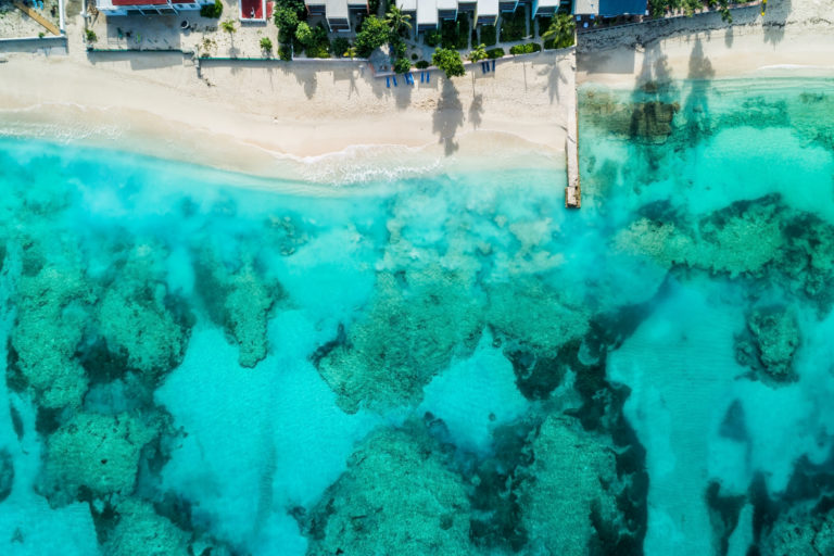 Beach with pier and coastline. Caribbean clear ocean water, coral reefs. Aerial view