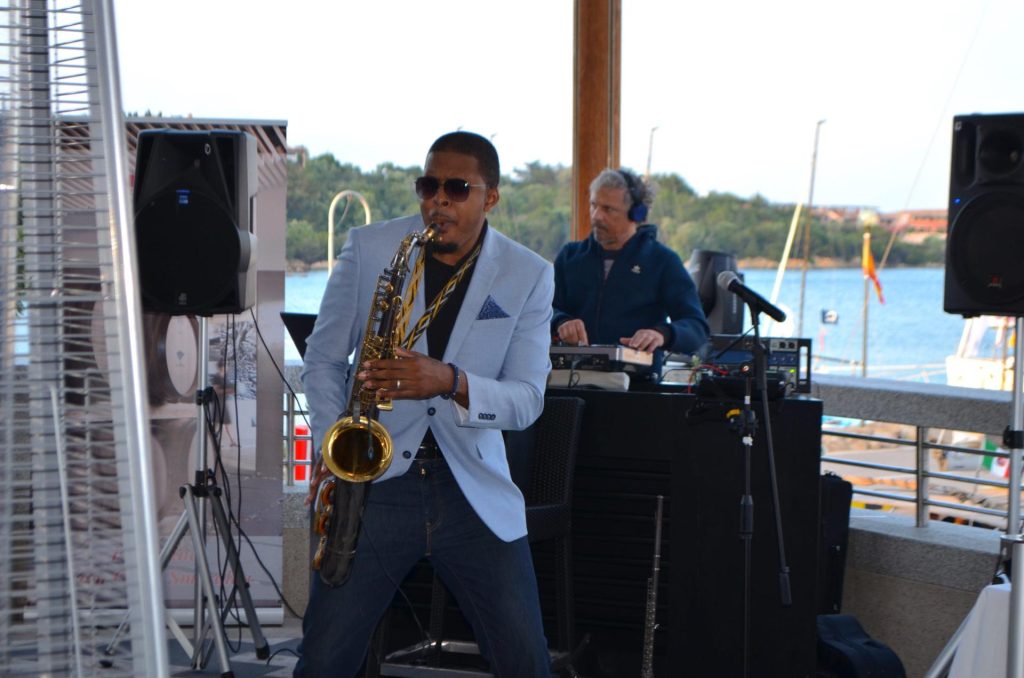 Sardinia, Mediterranean Amau Georges plays saxophone with DJ Max in background on Sailing Regatta  - High Point Yachting